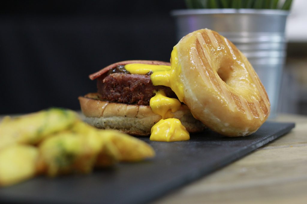 Nuevos platos veganos. Vegan Donut Burger: Bacon vegano, quesos havarti y cheddar veganos fundidos, cebolla caramelizada y lo mejor, ¡sustituimos el pan superior por un esponjoso Donut vegano!